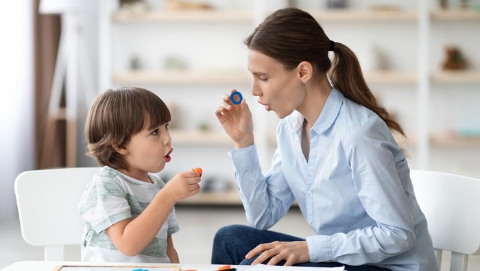 Female speech therapist curing child's problems and impediments. Little boy learning letter O with private English language tutor during lesson at office