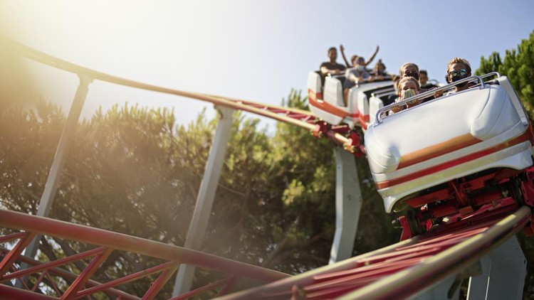 1269729482 Kids having fun in a small roller coaster in amusement park. Kids are enjoying the ride on a sunny summer day. COVID-19 pandemic. Everyone is wearing face masks. The ride details and color altered in post processing