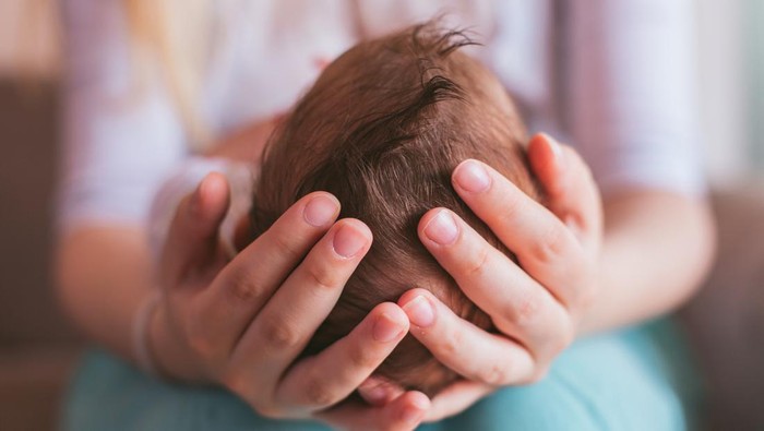 Mother holding newborn baby boy on her knees, closeup