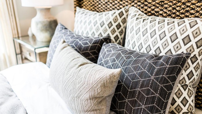 Closeup of new bed comforter with decorative pillows, headboard in bedroom in staging model home, house or apartment
