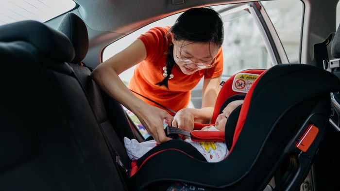 Image of an Asian Chinese woman fastening seat belt for her baby boy on car safety seat before driving