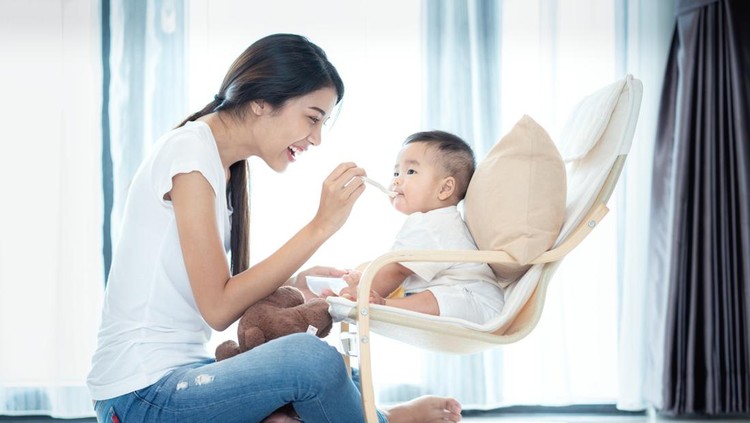 IIlustrasi Penyebab Berat Badan Bayi MPASI Sulit Naik Asian mother feeding to her baby in leving room