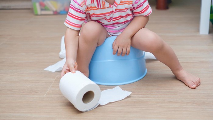 Closeup of legs of little Asian 2 years old toddler baby boy child sitting on blue potty holding, playing with toilet paper. Potty training, Learning to use the Toilet concept - Soft & Selective focus