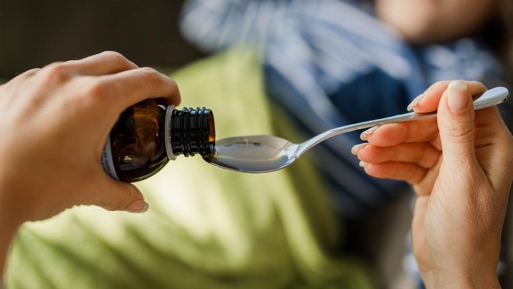 Close up of unrecognizable single mother pouring syrup into the spoon for her sick child.