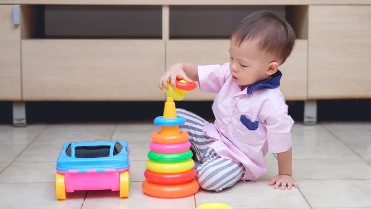 Cute little Asian 18 months / 1 year old toddler boy play with educational colorful plastic pyramid toy / stacking ring toy in living room, Early Childhood Development of Fine Motor Skills concept