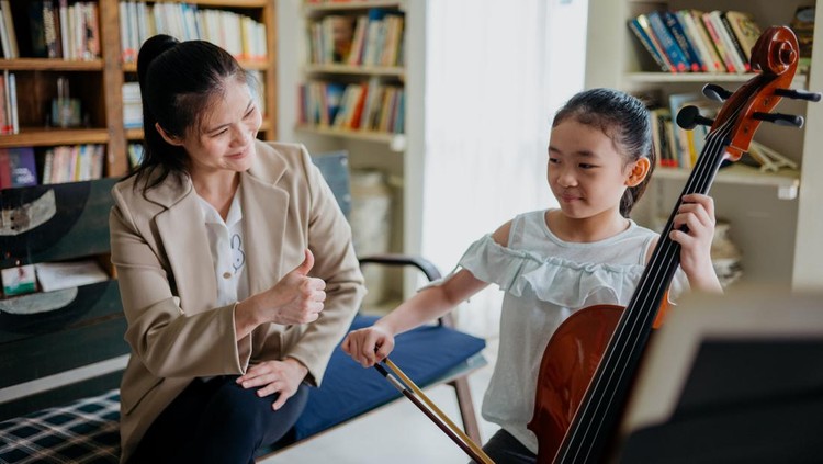 Little girl playing cello at home with music teacher, receiving thumb up priase