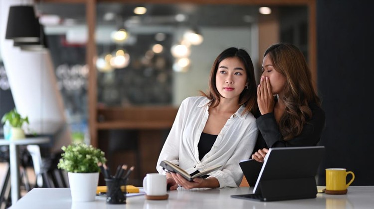 Business woman whispering something  in ear of her colleague.