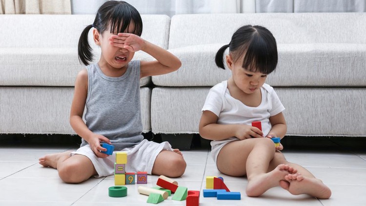 Asian Chinese little sisters struggle for blocks on the floor in the living room at home.