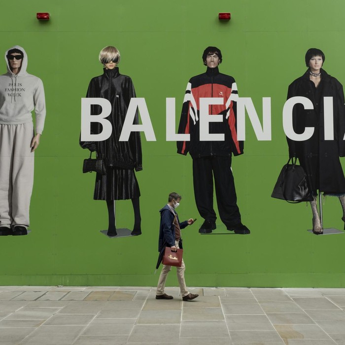 People interact with large scale action figures wearing fashionable clothing against a huge green hoarding which covers the Balenciaga store during a refit in the upmarket area on Bond Street on 25th May 2021 in London, United Kingdom. These high end brands are seen next to each other on a very ordinary wall. Bond Street is one of the principal streets in the West End shopping district and is very upmarket. It has been a fashionable shopping street since the 18th century. The rich and wealthy shop here mostly for high end fashion and jewellery. (photo by Mike Kemp/In Pictures via Getty Images)