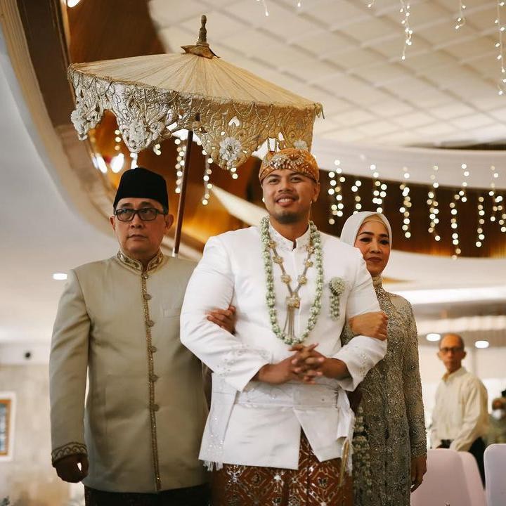 <p>Serasi dengan Obit, Dimas juga mengenakan pakaian pengantin berwarna putih, Bunda. Kebahagiaan pun terpancar saat ia memasuki ruangan bersama kedua orang tua. (Foto: Instagram: @zanacobhita)</p>