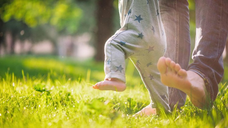 Father helping his baby boy to make first steps on green grass