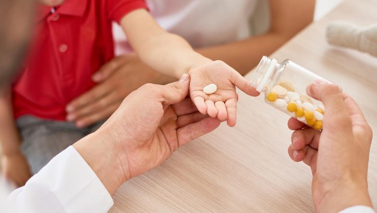 Close-up shot of unrecognizable pediatrician giving vitamins to little patient sitting on laps of his mother