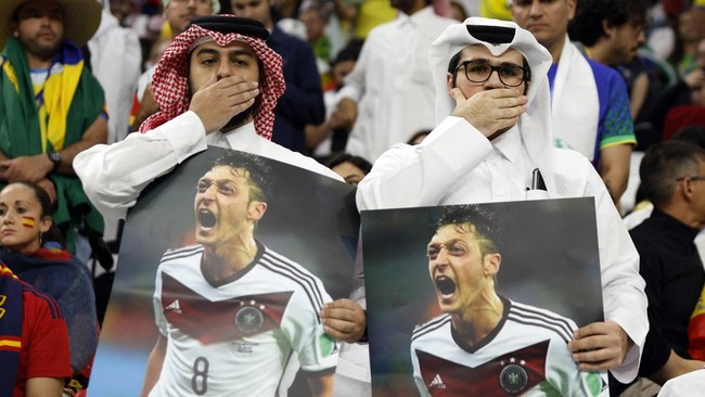 Fans Qatar memegang poster Ozil sambil menutup mulut untuk membalas aksi Jerman di Piala Dunia 2022.