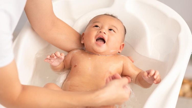 Ilustrasi Rekomendasi Sabun Bayi Calm of asian newborn baby bathing in bathtub.mother bathing her son in warm water.Happy adorable newborn infant smile in tub relax and comfortable.Newborn baby care concept