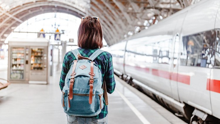 A young tourist girl with backpack waits for train on railway station