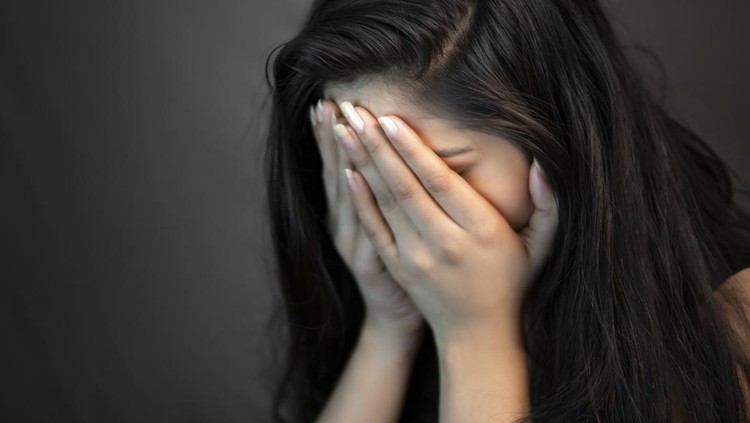 1308413743 Close-up portrait of alone, stressed young woman sitting in darkness and crying with covering her face with hands.