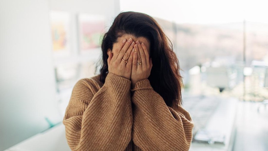 Portrait of a shy young woman in her loft apartment&comma; covering her face with her hands