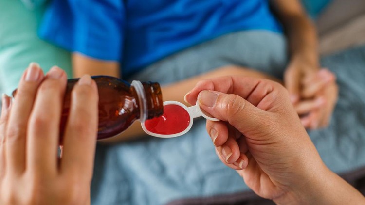 Ilustrasi Daftar Obat Aman untuk Anak Menurut BPOM Woman's hand pouring syrup for sick child.