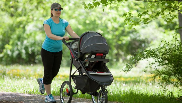 Young mother running while pushing a stroller in the park