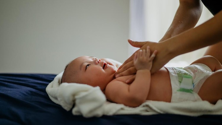 Ilustrasi Teknik Memijat Bayi Image of an Asian Chinese woman applying baby cream and massaging her baby boy after bath