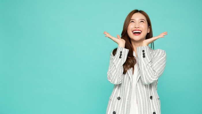 Young beautiful Asian woman surprise and look up at the empty space above isolated over green background, Thrilled excited concept