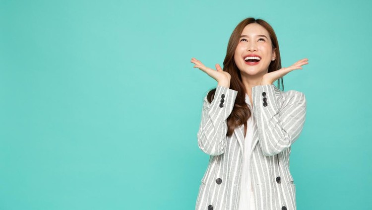 Young beautiful Asian woman surprise and look up at the empty space above isolated over green background, Thrilled excited concept
