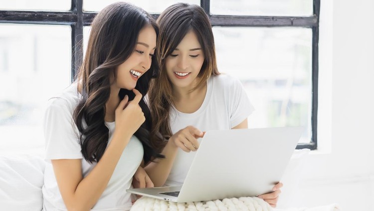 1402419223 Two beautiful asian women using laptop computer talking and smiling while sitting on bed at home Happy girls using laptop for Internet and social media Beautiful young lady enjoy using laptop computer
