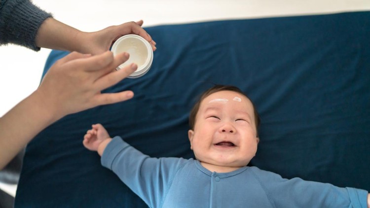 Applying moisturizing cream on face of baby
