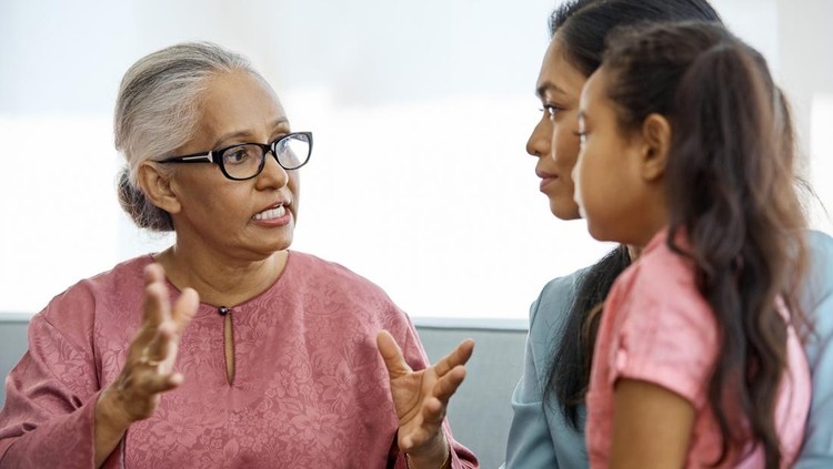 958689770 Senior woman gesturing while talking to females at home. Multi-generational family sitting on sofa. They are wearing casuals.