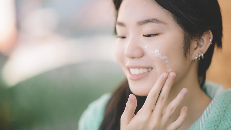 an asian chinese teenager girl applying moisturiser facial cream on hand and face