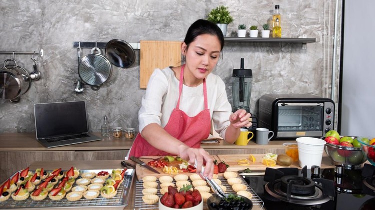 Asian woman making fruit tart for online selling delivery. Female small business bakery shop owner entrepreneur working in laptop computer get order for customer. Small business work at home concept.