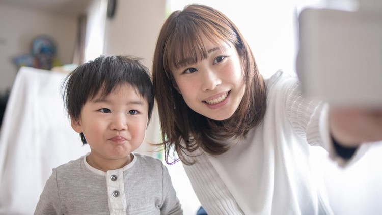 Young mother and son taking selfie picture in living room
