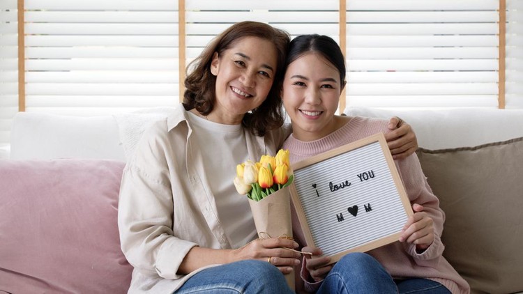 hadiah hari ibu Attractive beautiful asian middle age mum sit with grown up daughter give gift box and flower in family moment celebrate mother day. Overjoy bonding cheerful kid embrace relationship with retired mom.