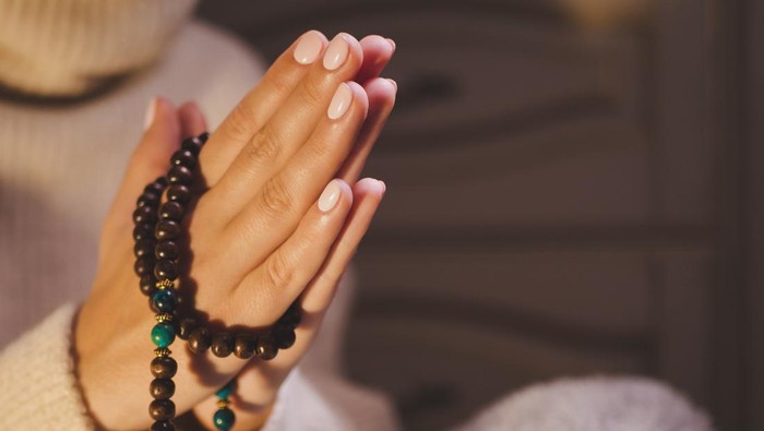 Concentrated woman praying wearing rosary beads. Namaste. Close up hands.