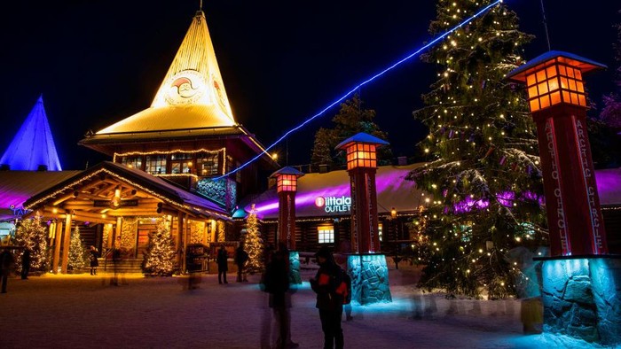 A picture taken on December 2, 2019 shows tourists next to a blue electric line at the Santa Claus Village that marks the border of the Arctic Circle near Rovaniemi, Finnish Lapland. - Rovaniemi's Santa Claus Village amusement park is a snow-covered wonderland of reindeer rides, ice castles, souvenir shops, snowmobiles and igloo hotels where Christmas holds sway 365 days a year. But Lapland is also the homeland of the indigenous reindeer-herding Sami people, who protest that some in the tourist industry spread offensive stereotypes about Sami people and seek to profit from their ancient culture. (Photo by Jonathan NACKSTRAND / AFP) (Photo by JONATHAN NACKSTRAND/AFP via Getty Images)