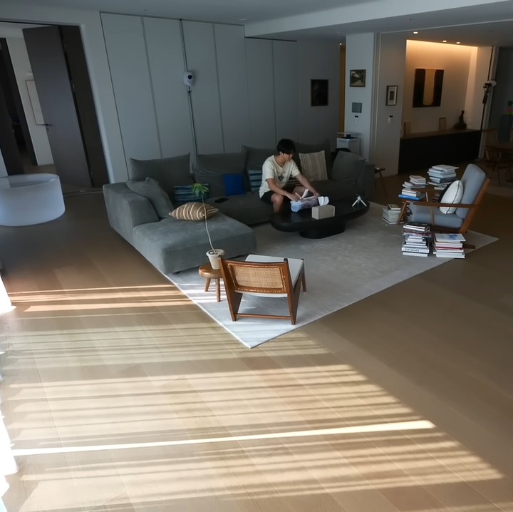 <p>Rumah RM BTS didominasi warna cokelat, hitam, dan putih. Selain itu, RM memang memiliki hobi membaca. Di ruang tamunya yang lega, ia menumpuk banyak buku di sekitar kursi membacanya. (Foto: YouTube/BANGTAN TV)</p>