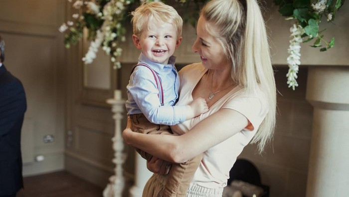 Mother holding her son while at a wedding reception. They are both smiling.