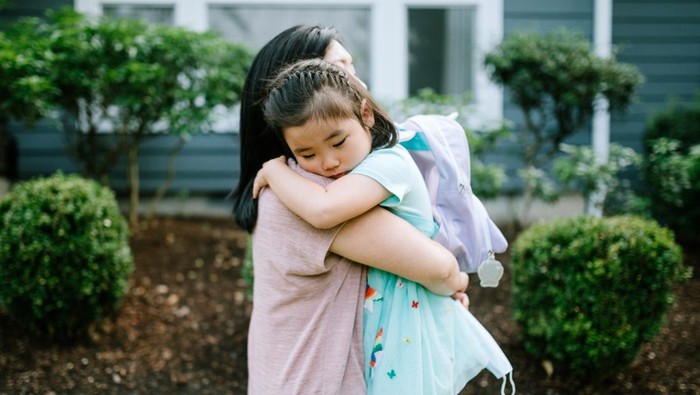 A Korean woman holds her daughter tightly in an embrace, the girl feeling anxious going back to school.