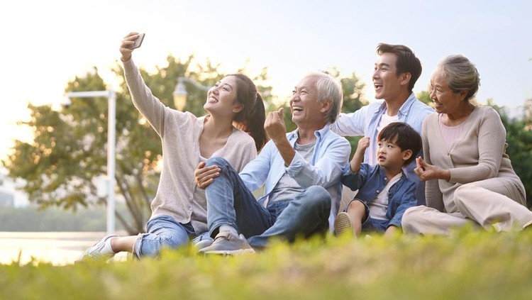 Ilustrasi Tempat Wisata Bersama Keluarga di Sentul three generation happy asian family sitting on grass taking a selfie using mobile phone outdoors in park