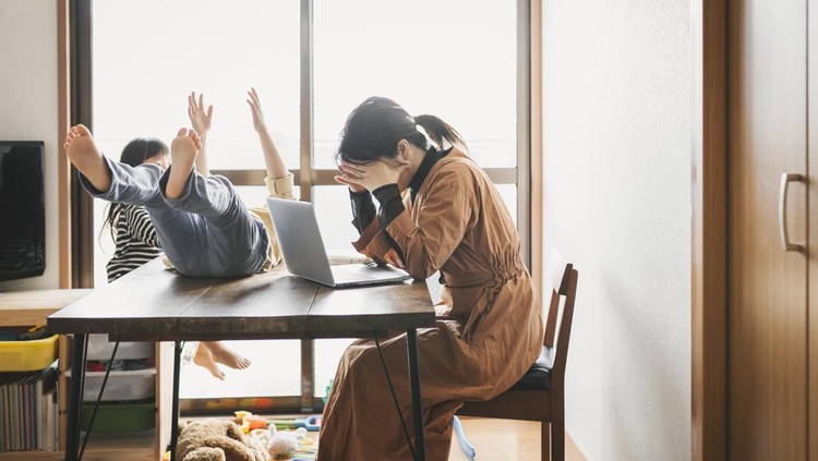 Asian mother working with laptop while her son and daughter are playing in the living room&period; Her son is playing on the table&period;