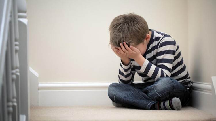 Upset problem child with head in hands sitting on staircase concept for childhood bullying, depression stress or frustration
