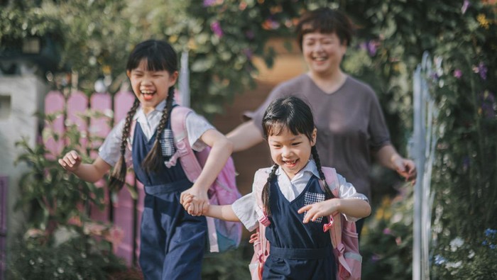 asian chinese mother sending both her daughters to school from home at front yard of house in the morning