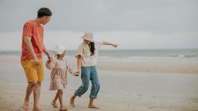 Southeast Asian parent cheers up their girl to explore stepping on the beach on vacation and seeking a beautiful view of the sea, Excitement with their experience