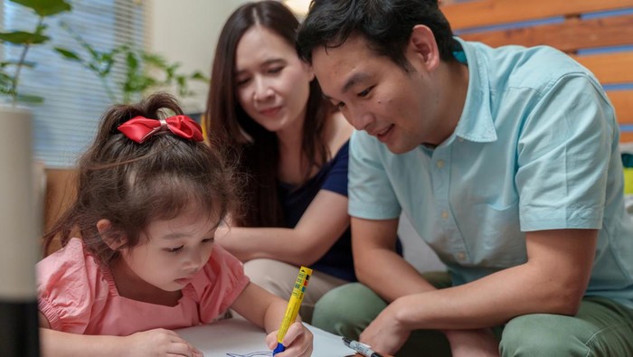 Asian little cute girl drawing and writing Christmas cards, preparing for celebrating Christmas and New year. Adorable girl focusing on her draws while making Christmas cards with her parents.