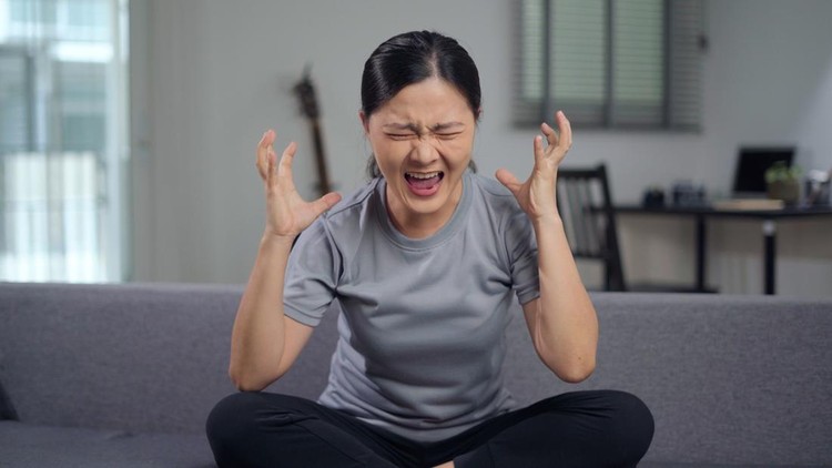 Asian woman angry seriously sitting on sofa in living room at home looking at camera and shouting.