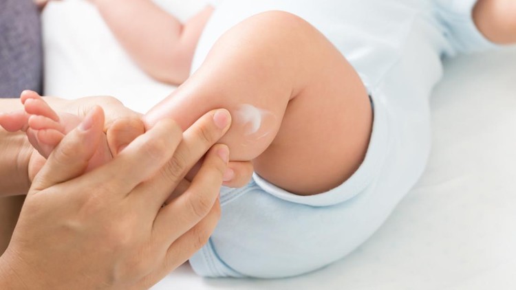 Mother is applying cream to the baby boy which helps to maintain skin leg hydration, Skincare and moisturizing cream concept