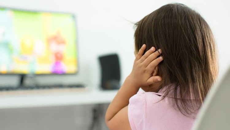 1134790265 A child watching tv holding her ears because she is afraid of the sound; Child behavior theme