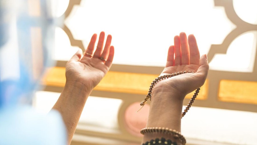Muslim woman in headscarf and hijab prays with her hands up in air in mosque.Religion praying concept.