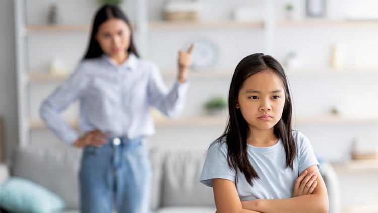 Family conflict. Mother and daughter quarreling at home, sulky child girl ignoring her mom, standing back to her with crossed arms, selective focus, copy space