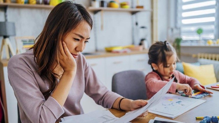 Young stressed mother checking her finances while her daughter is playing next to her